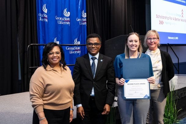 Elizabeth holding a presentation award certificate with three event representatives